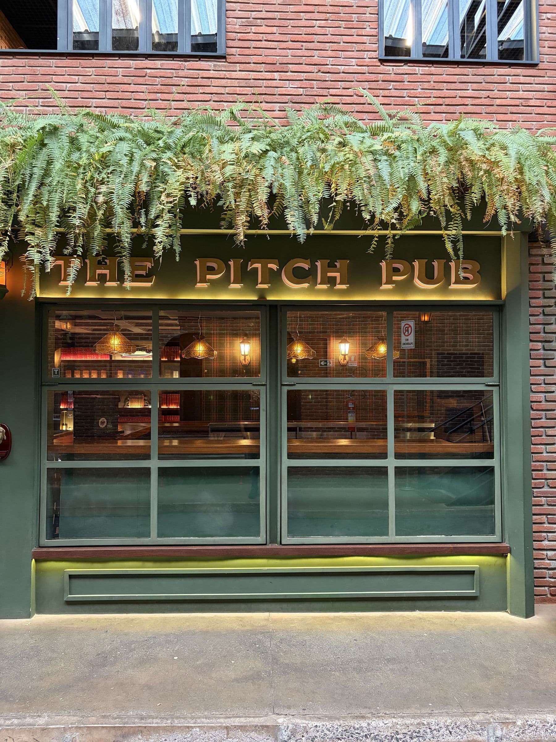 A fachada do The Pitch Pub: o letreiro dourado sobre as janelas de moldura verde, com samambaias caindo da jardineira.